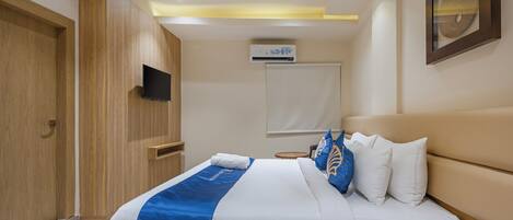 Una habitación de hotel con cama, mesita de noche, teléfono, aire acondicionado y televisor montado en la pared.