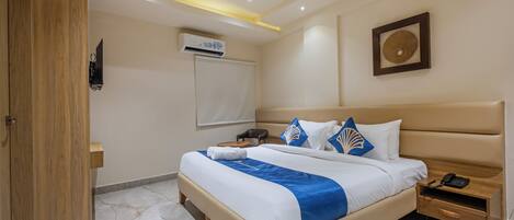 A hotel room with a large bed, bedside tables, a desk, an air conditioning unit, and a wall-mounted artwork.
