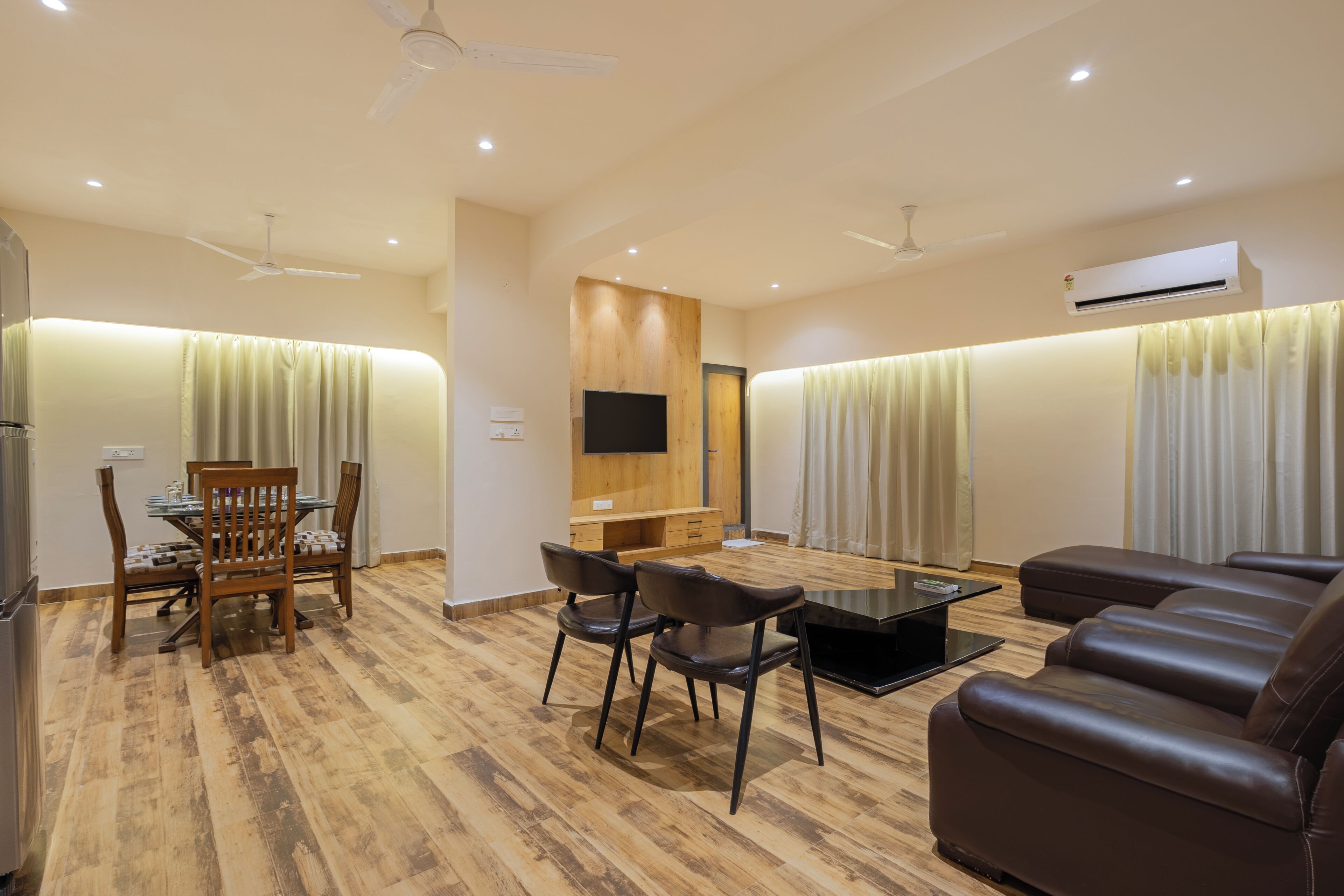 A modern living room with a dining area, wooden flooring, a flat-screen TV, and a leather sofa.