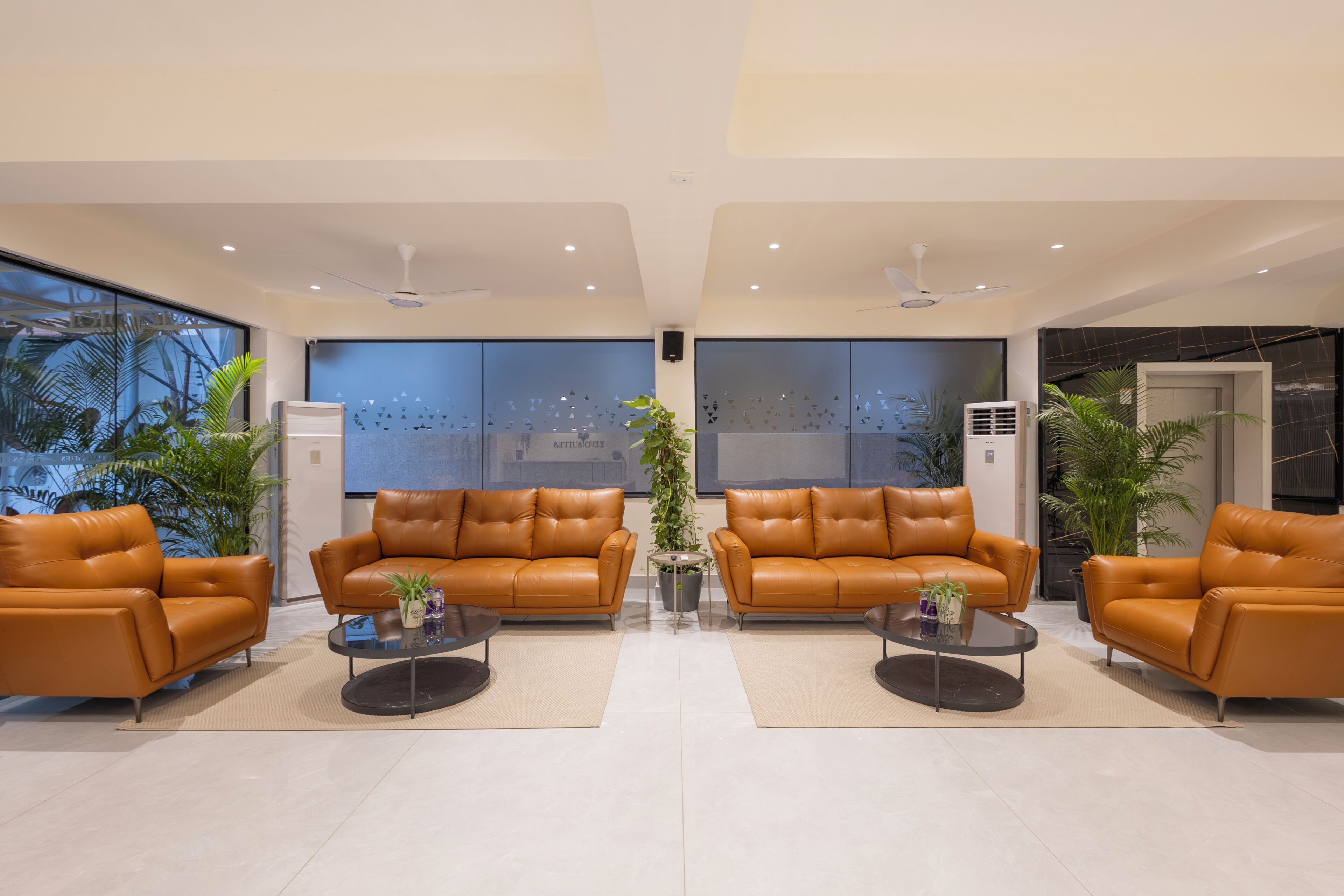 A modern lobby with leather sofas, a glass coffee table, and potted plants.
