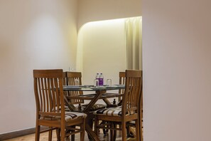 Un coin repas avec une table ronde et quatre chaises en bois, un plateau en verre et deux bouteilles d’eau.