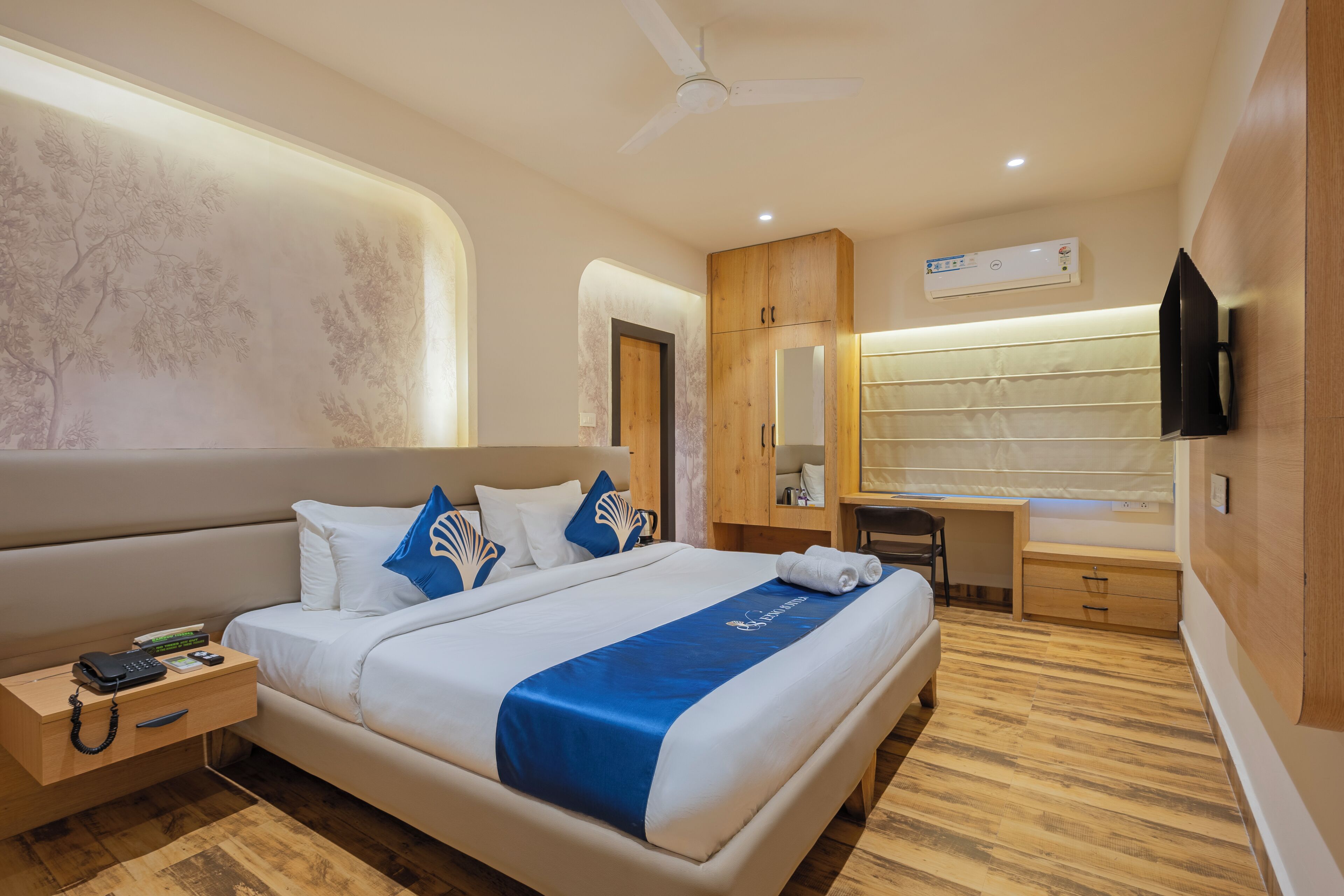 Een moderne hotelkamer met een groot bed, een bureau, een stoel, een flatscreen televisie en een plafondventilator.