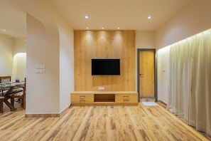 Una sala de estar moderna con un mueble de madera para entretenimiento, un televisor de pantalla plana y una zona de comedor con mesa y sillas.
