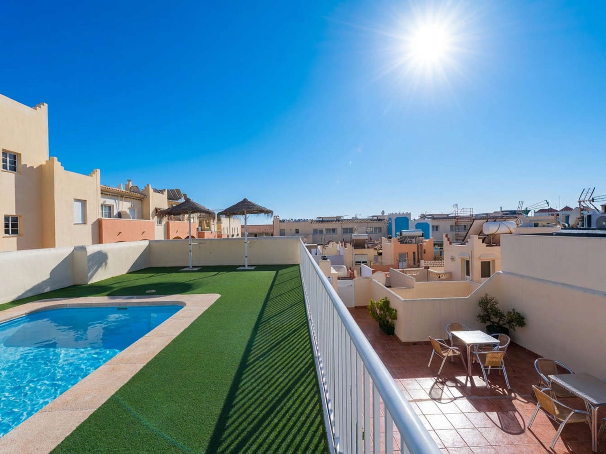 A rooftop with a swimming pool, artificial grass, and outdoor furniture.