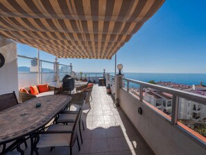 Um terraço com toldo xadrez, mobiliário de exterior e vista para o mar.