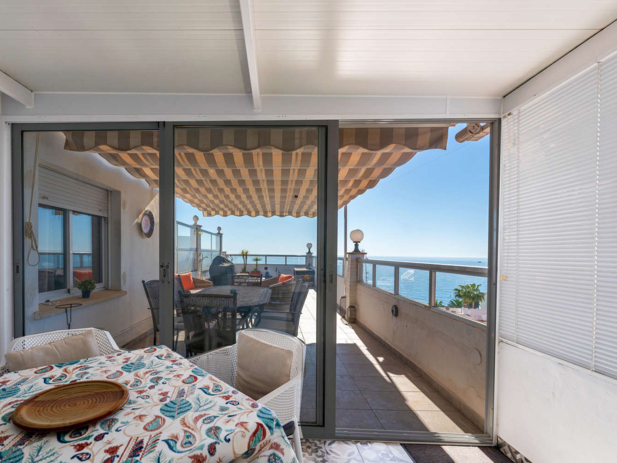 Un balcon avec une table et des chaises, une vue sur la mer et une nappe à motifs.