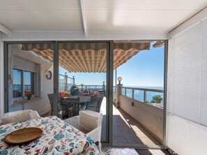 Uma varanda com mesa e cadeiras, vista para o mar e toalha de mesa estampada.