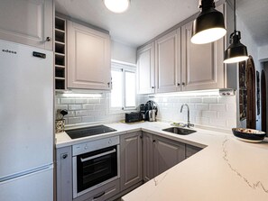 A modern kitchen with white cabinets, a stainless steel refrigerator, a built-in oven, a microwave, and a sink. - Apartment  by Interhome (Nerja)