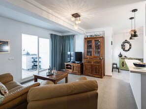 A living room with a sofa, a coffee table, and a television. There is a cabinet with glass doors and a dining area with a table and chairs. - Penthouse Seaview Centro by Casasol by Interhome (Nerja)