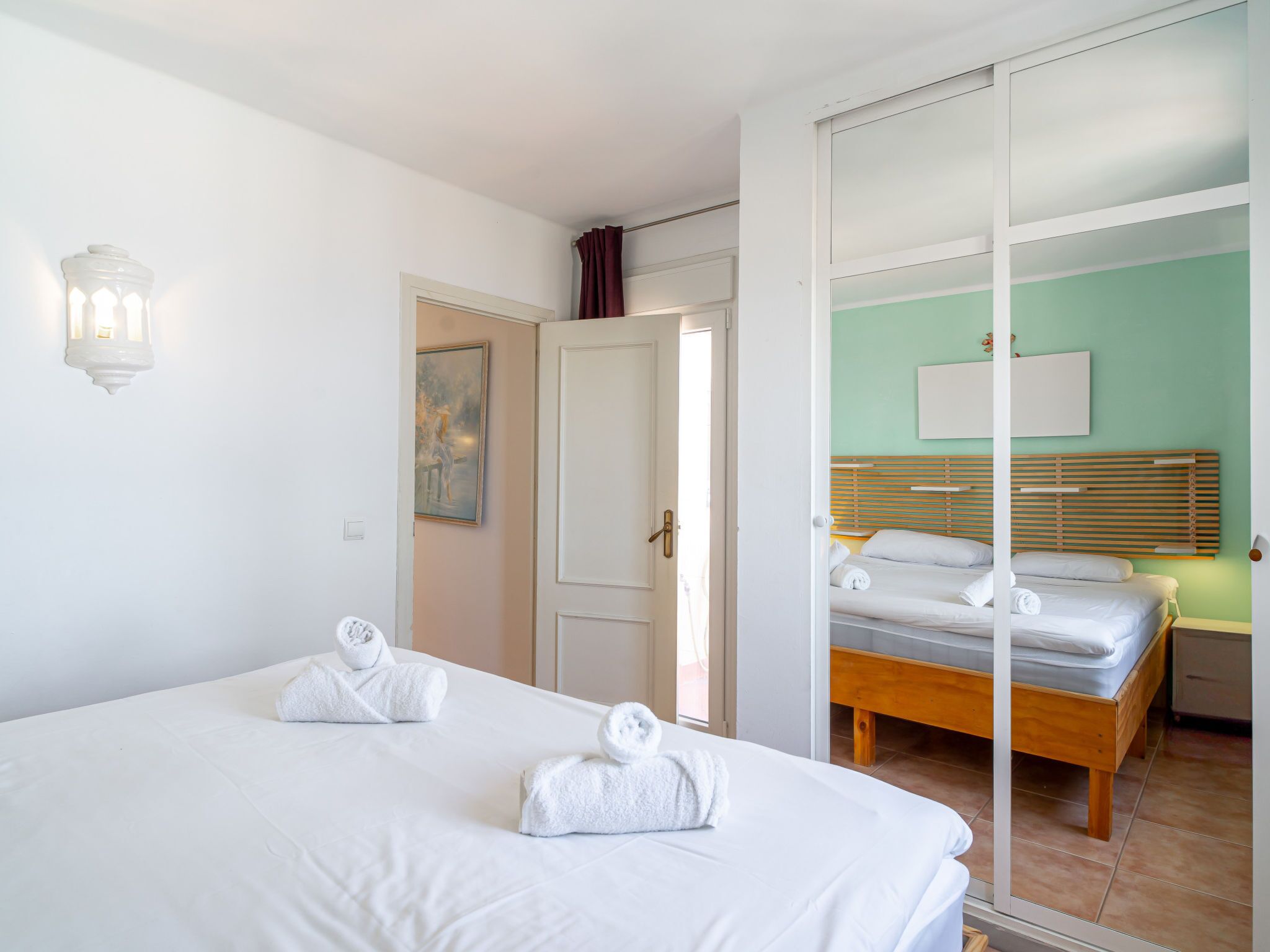 A hotel room with two beds, a sliding door, a painting, and a wall-mounted light fixture.