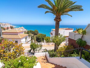Zona residencial costera con vista despejada al mar, una palmera y una escalera que conduce a un edificio con techo de tejas.