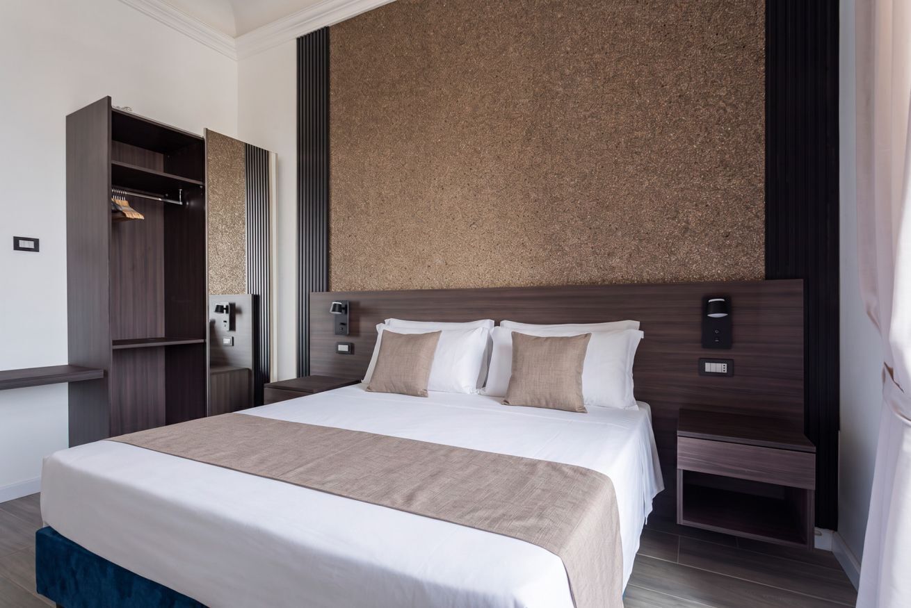 Una camera d'albergo con un letto grande, un armadio, un comodino e una lampada a parete.
