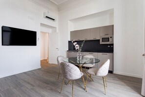 Een moderne keuken met een flatscreen televisie, een eethoek met een glazen tafel en comfortabele stoelen, en een zichtbare deur die naar een andere kamer leidt.