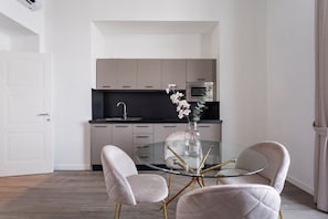 Una cucina moderna con un tavolo rotondo in vetro e due sedie, una porta bianca e un vaso con fiori.