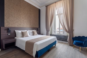 Una camera d'albergo con un letto grande, un comodino, una poltrona blu e vista dalla finestra.