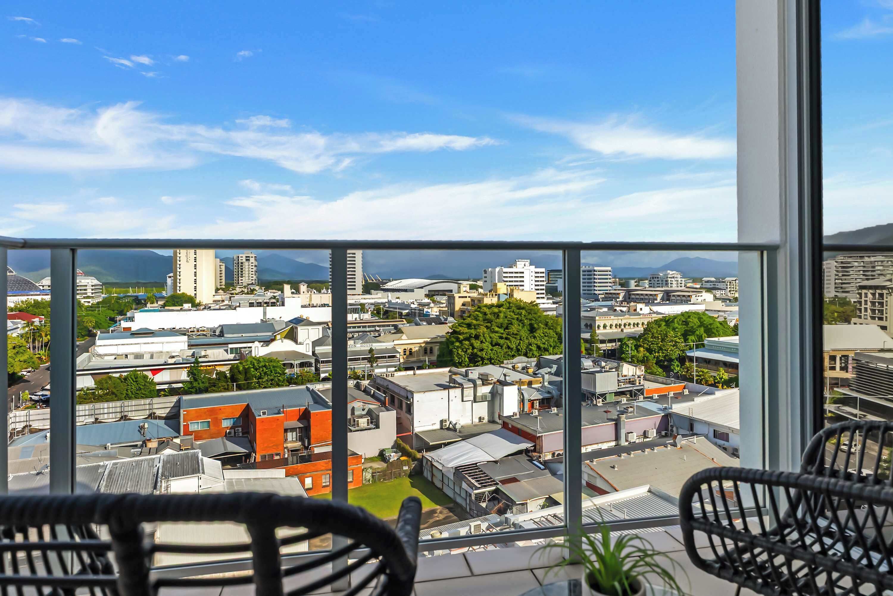 Ein Hotelzimmer in einem Hochhaus mit Balkon und Blick auf eine Stadtlandschaft, mit blauem Himmel und fernen Bergen.