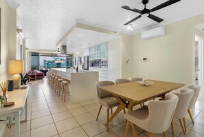 A modern kitchen with a central island, a dining area with a wooden table and chairs, and a ceiling fan. - Seaview Escape—Scenic Views, Pool and Prime Location (Cairns City)