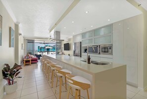 A modern kitchen with a central island, bar stools, and a dining area with a sofa and chairs. - Seaview Escape—Scenic Views, Pool and Prime Location (Cairns City)