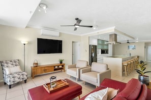 Ein modernes Wohnzimmer mit Flachbildfernseher, einer Holzkommode, einem roten Sofa und einer Küchenzeile mit Kühlschrank und Barhocker.