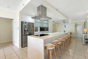 A modern kitchen with a central island, stainless steel appliances, and a bar area with stools. - Seaview Escape—Scenic Views, Pool and Prime Location (Cairns City)