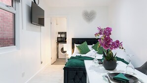 A modern bedroom with a bed, a dining table with chairs, a TV mounted on the wall, and a kitchen area visible through an open door. - Modern studio on Thornton heath station just 5minutes away offering train to cit (Thornton Heath)