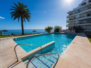 A swimming pool with a clear view of the ocean, a palm tree, and a multi-story building with balconies. - Acapulco Playa 302 by Casasol by Interhome (Nerja)