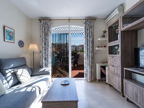 Sala de estar com sofá, mesa de centro e aparador para TV. Uma porta de vidro deslizante dá acesso a uma área externa.