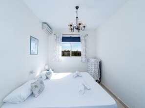 Ein Schlafzimmer mit Bett, einem Fenster mit Vorhängen, einer Kandelaber und einer Klimaanlage.