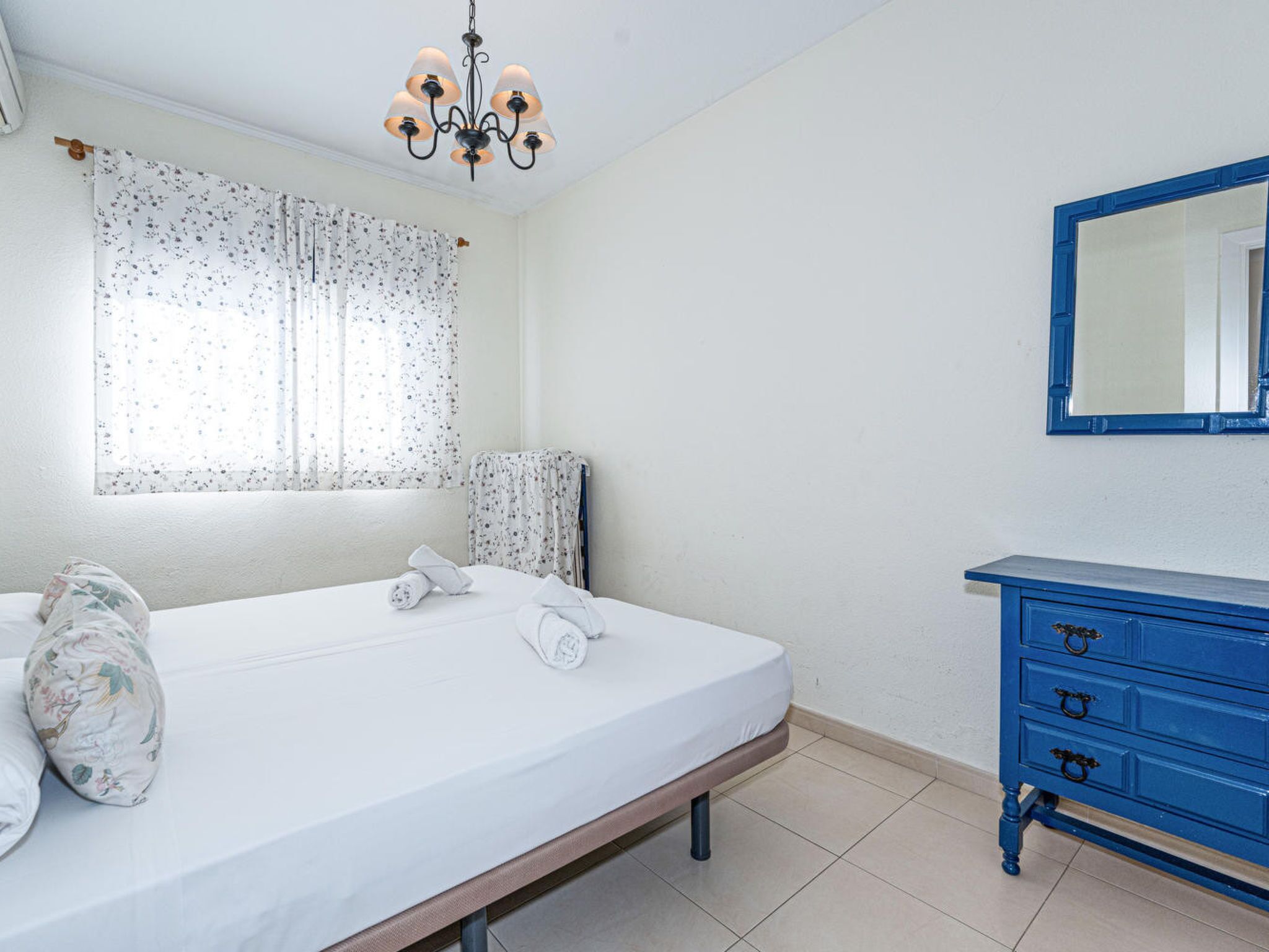 Ein Schlafzimmer mit einem Bett, einer blauen Kommode, einem Spiegel und einer Pendelleuchte.