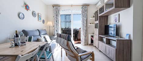 A compact living space with a dining area, sofa, TV, and a balcony with a view.