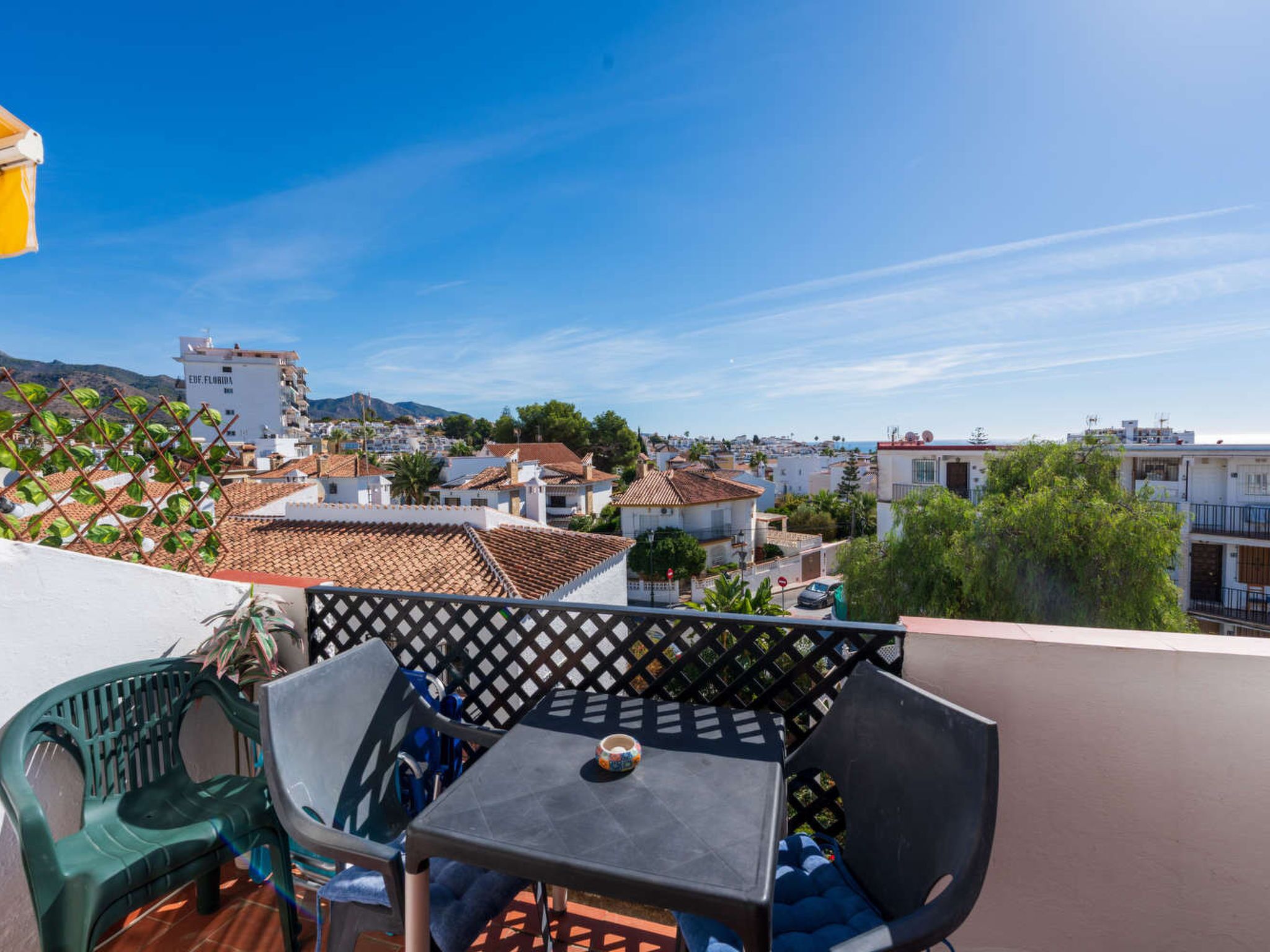 Un balcón con mesa y sillas, con vistas a una zona residencial con edificios y cielo despejado.