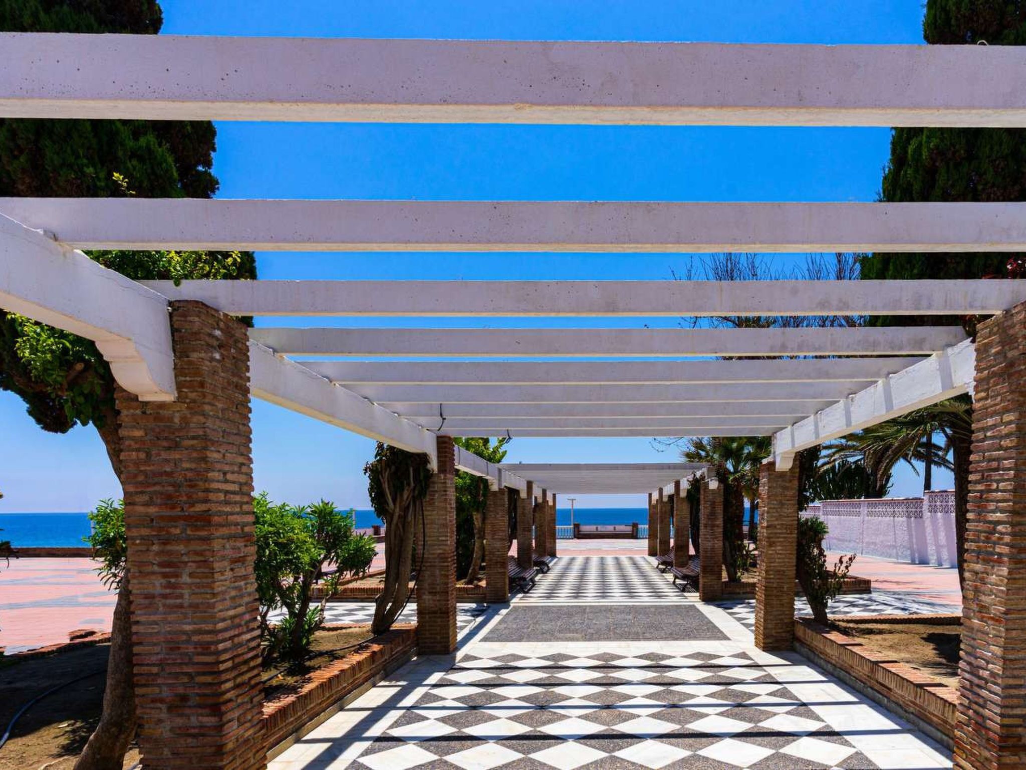 A covered walkway with a checkered floor leading to a view of the sea.