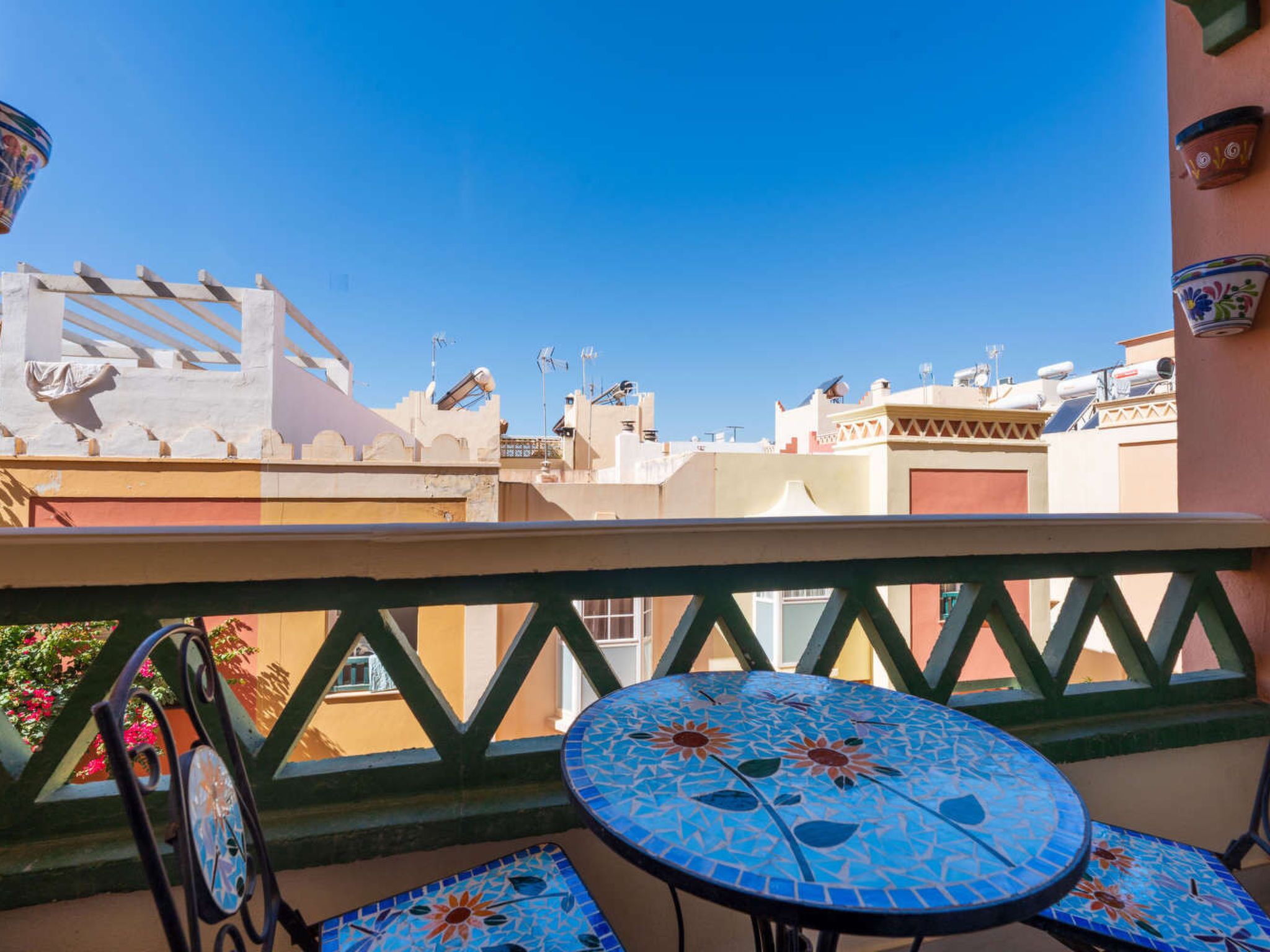 A balcony with a tiled table and chairs, overlooking a cityscape with buildings and a clear sky.