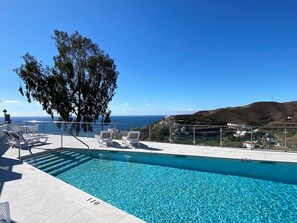 Ein klares, blaues Schwimmbecken mit Liegestühlen und Blick auf das Meer und die Hügel.