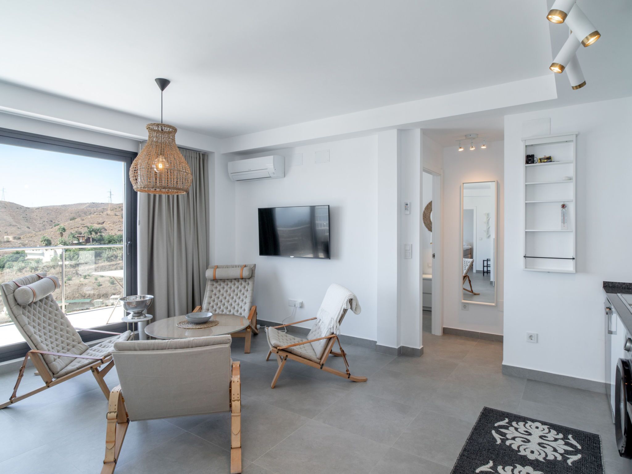 A modern living room with a large window, a flat-screen TV, and a dining area with a round table and chairs.