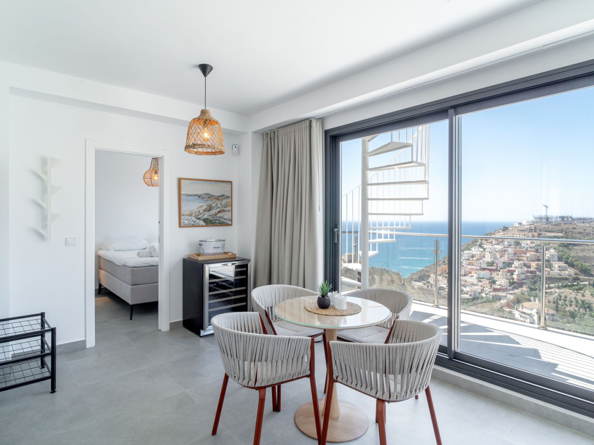 A modern living room with a dining area, large windows, and a view of the sea.