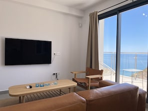 A modern room with a flat-screen TV mounted on the wall, a wooden table with glasses, a leather sofa, and a balcony with a view of the sea. - Penthouse Balcon del Mar Deluxe 3 by Casasol by Interhome (Nerja)