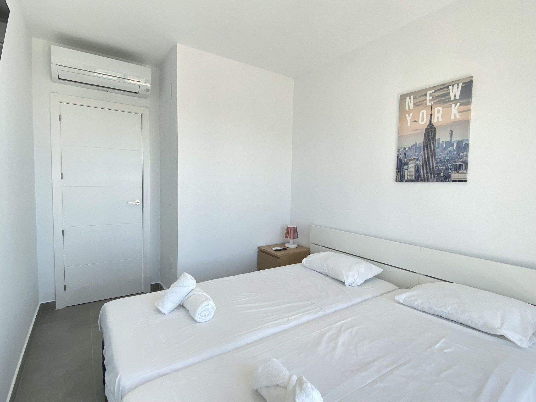 A hotel room with a bed, a nightstand, a lamp, and a poster on the wall.