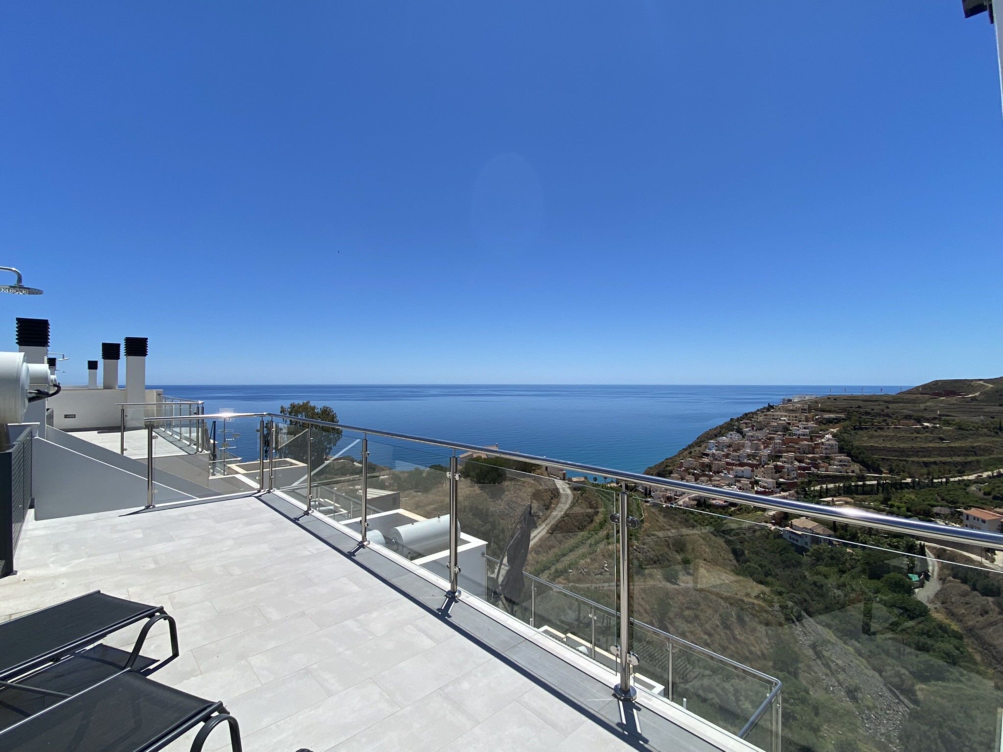 A rooftop terrace with a clear view of the sea and a hilly landscape.