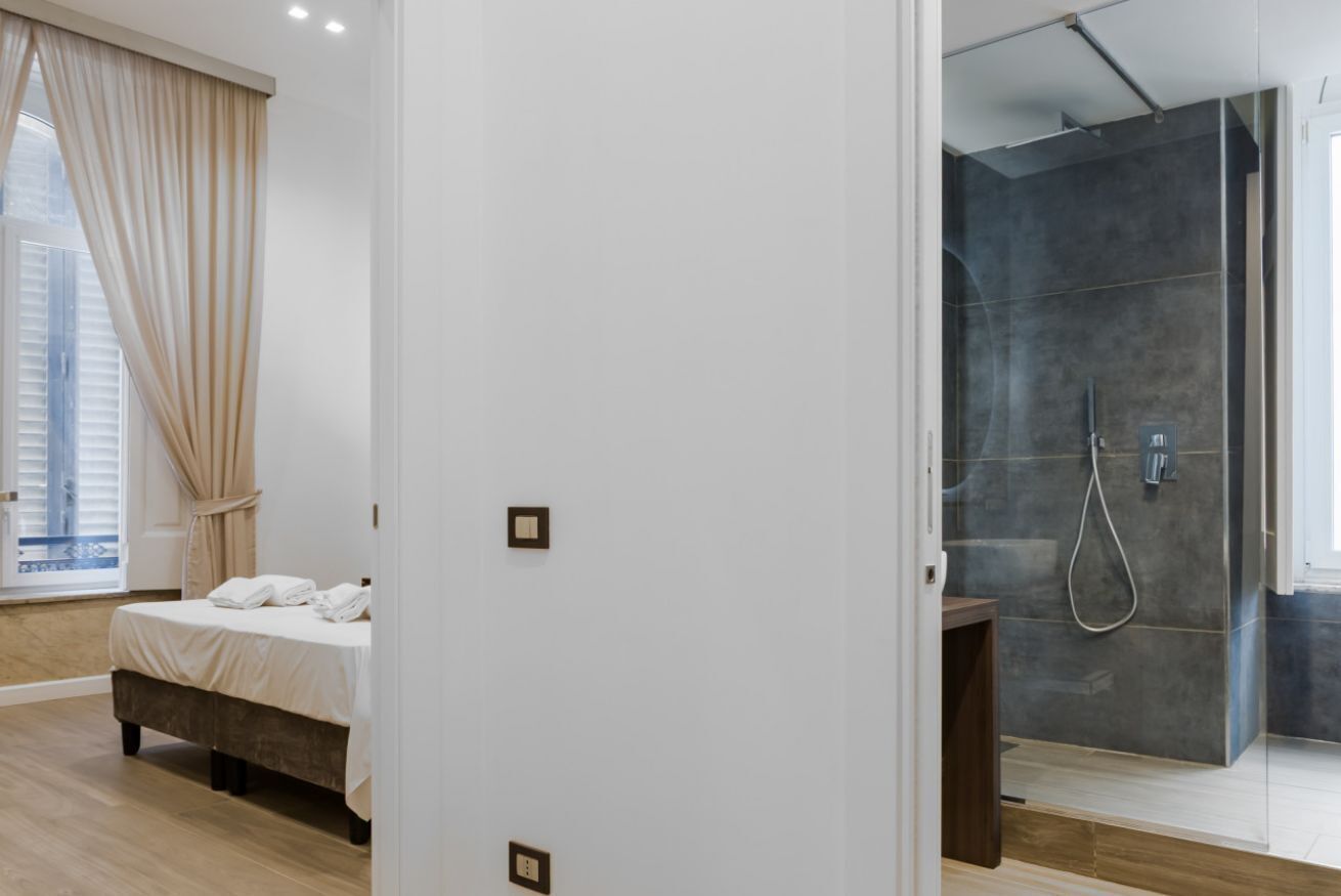 Une chambre à coucher avec un lit, une fenêtre avec des rideaux et un espace douche doté d’une porte en verre.