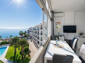 A balcony with a view of the sea and a pool, a dining area with a table and chairs, and a flat-screen TV on the wall. - Carabeo 45 Studio by Casasol by Interhome (Nerja)