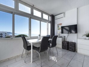 A modern dining area with a table and chairs, a flat-screen TV, and a view of the sea. - Carabeo 45 Studio by Casasol by Interhome (Nerja)