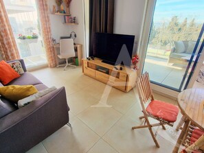 A living room with a sofa, a television on a wooden stand, a wicker chair, and a balcony with a view. - 104 / T2 RES DE STANDING, CLIM, PARKING (Sète)