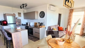 Et moderne køkken med en central ø, et spiseområde med træmøbler, og en stue med sofa og sofabord.