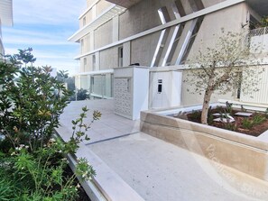 Un edifici modern amb teulada plana, una petita zona de jardí amb un arbre i una porta blanca.