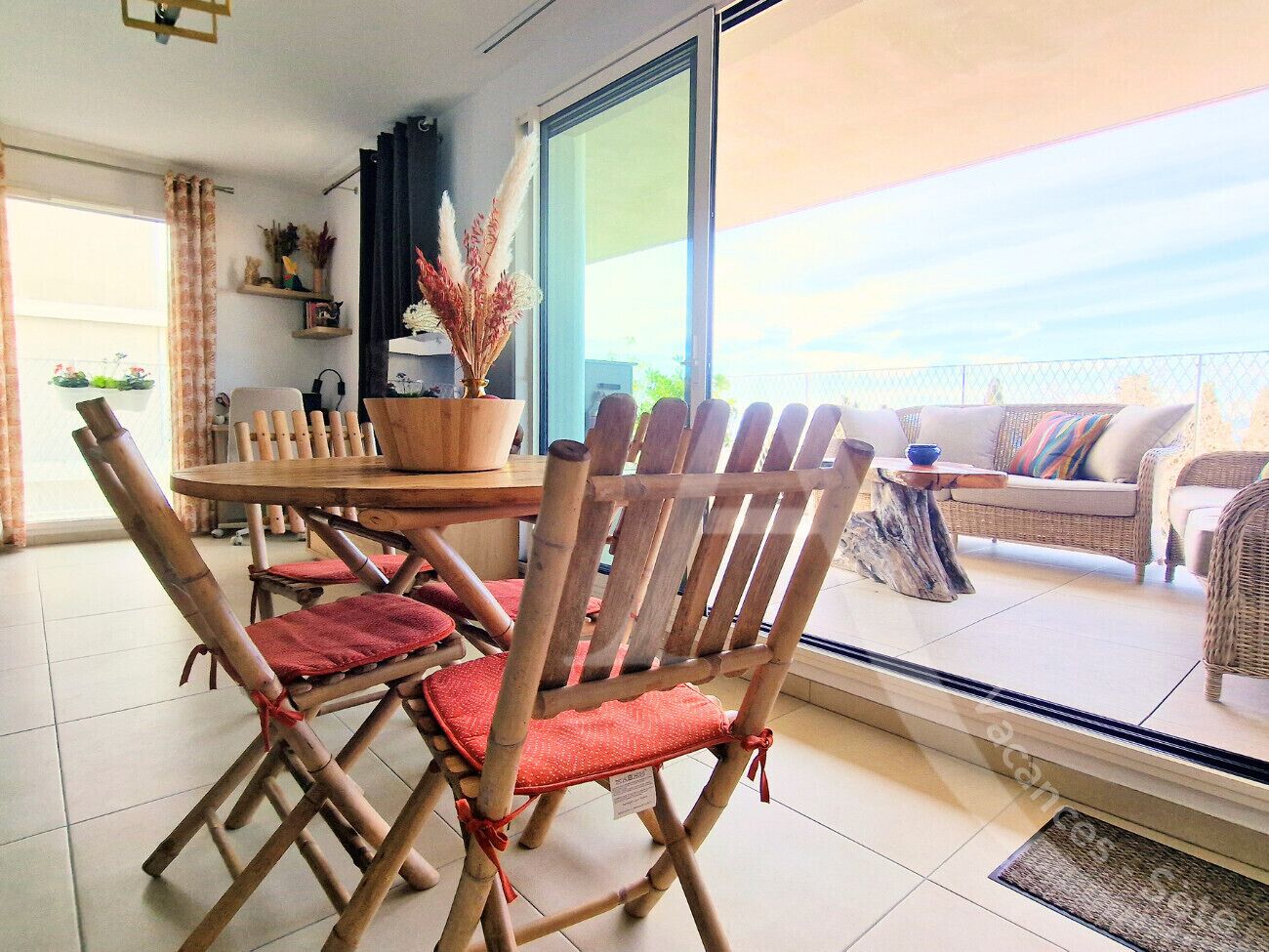 A dining area with bamboo chairs and a round table, a sofa with cushions, and a view through a glass door.