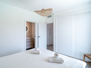 Een minimalistische slaapkamer met een groot bed, twee handdoeken, een hanglamp en een kledingkast.