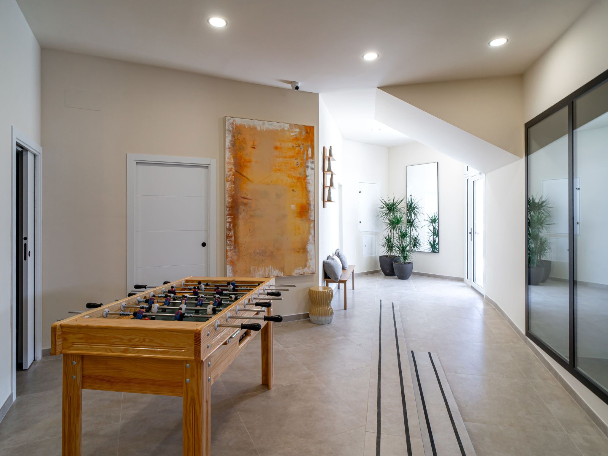 A spacious room with a foosball table, a large abstract painting, and a potted plant.