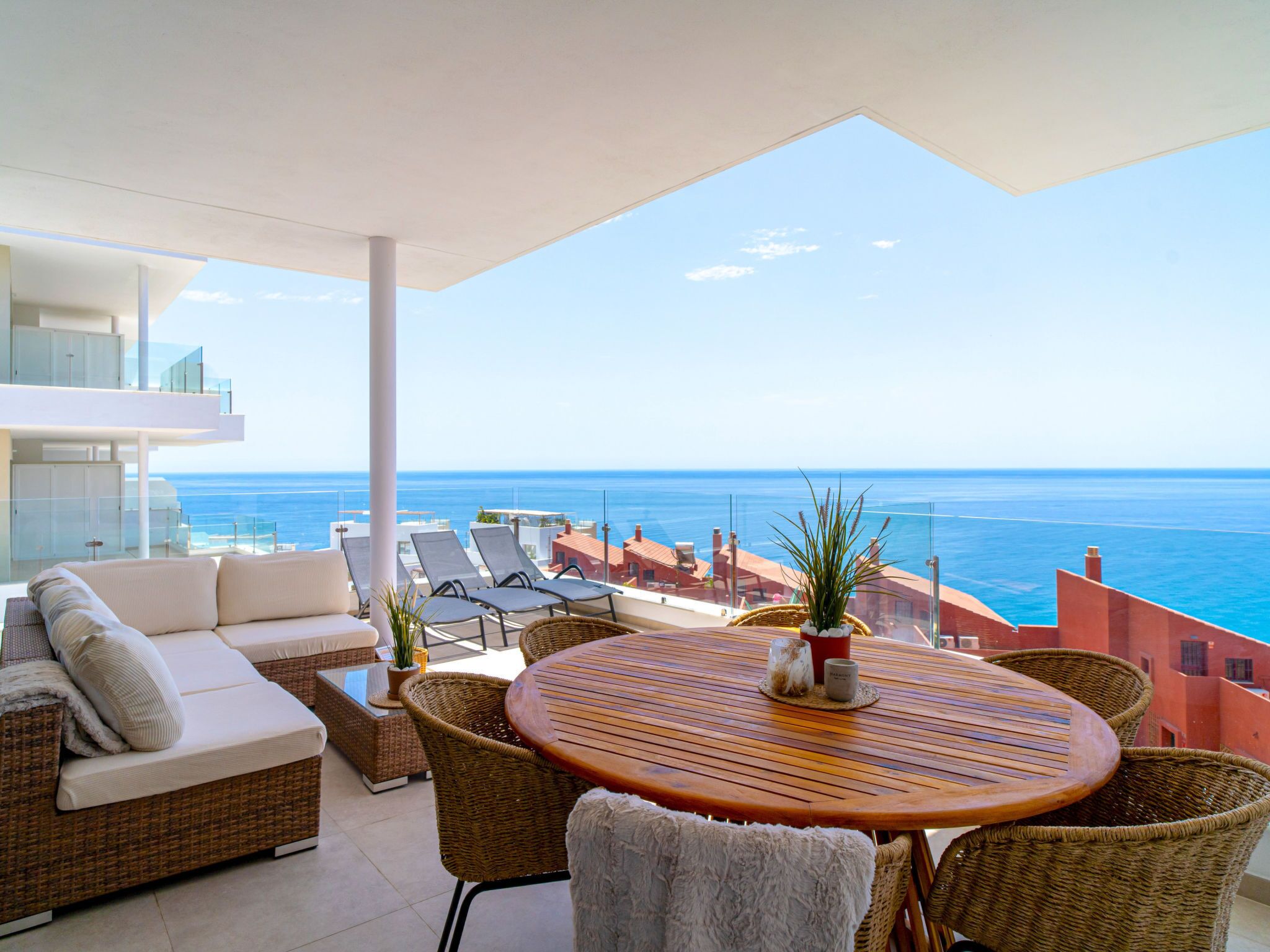 A balcony with a view of the sea, furnished with a sofa, chairs, and a table.