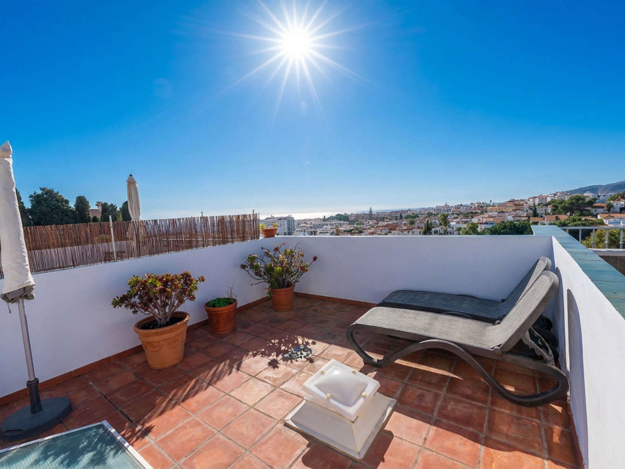 Eine Dachterrasse mit Liegestuhl, Pflanzkübeln und Blick auf die Stadt.